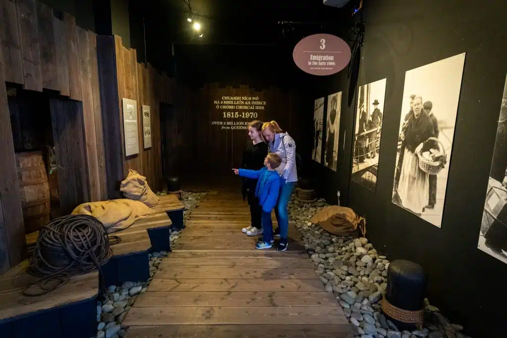 Two children explore an interactive display at a museum exhibition about immigration, featuring historical replicas and informational panels on the walls.