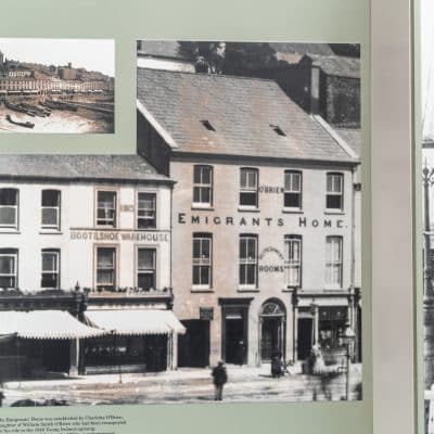 A historical display featuring a prominent photograph of the emigrants home building and a smaller inset image showing a busy riverside scenery. notable details include period architecture and vintage attire of people.