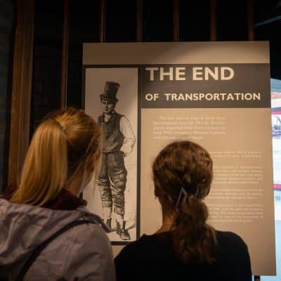 Two people viewing an exhibit panel titled "the end of transportation," featuring an image of a man in historical attire, at a museum.