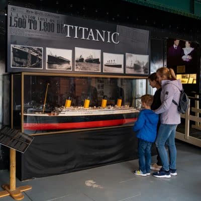 A family examines a large model of the titanic displayed under informational banners in a museum setting.