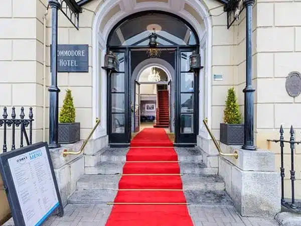 Entrance of the d' moore hotel with a red carpet leading to an open doorway, framed by topiary plants and a menu board on the left.