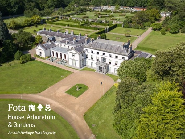 Aerial view of fota house, a large, elegant white building with a red roof, surrounded by extensive, meticulously maintained gardens and lush greenery. a gravel driveway leads to the house.