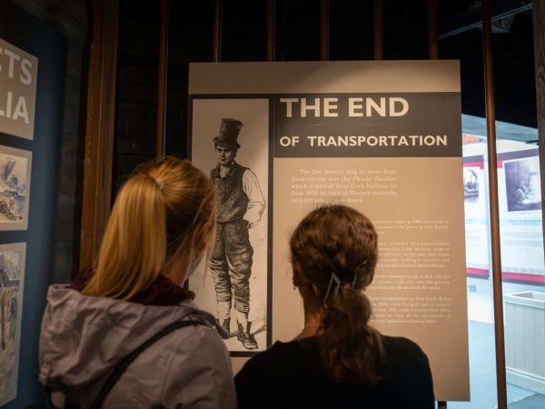 Two people viewing an exhibition panel titled "the end of transportation" about historic convict transportation to australia, displayed in a museum setting.